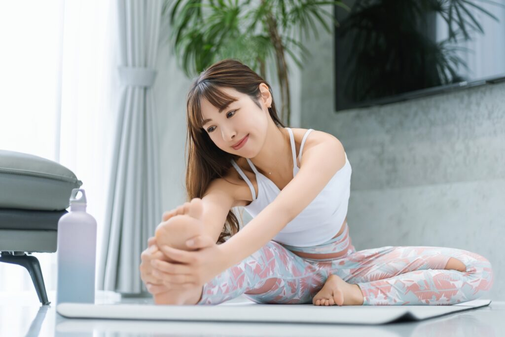 自宅のリビングでヨガマットに座り、足のストレッチをする女性