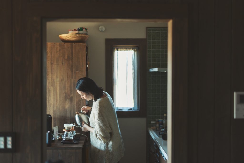 朝日が差し込むキッチンで、女性がカップにコーヒーを注いでいる様子。静かで穏やかな朝の豊かさを表している。