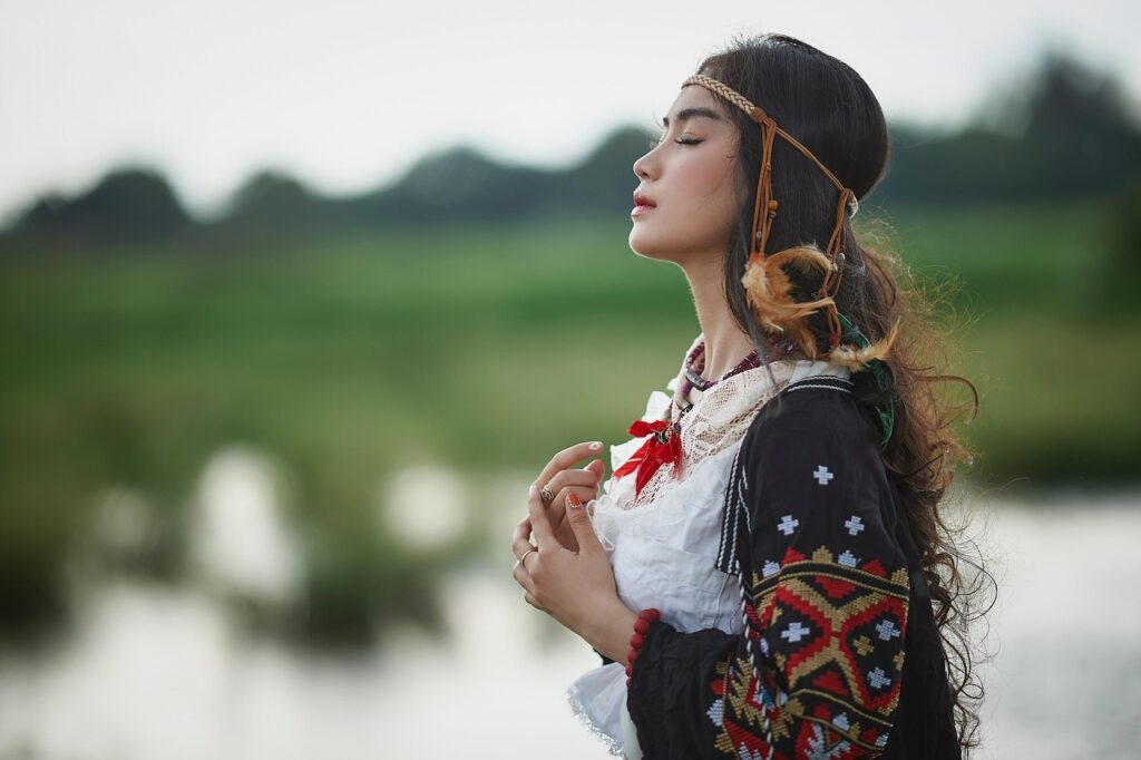 大自然の中で、女性が胸に手を当てて目を閉じ、静かに深呼吸している様子。心の落ち着きと内側の安らぎを象徴するイメージ。