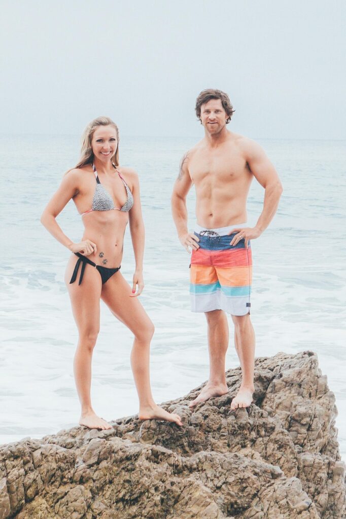 水着姿の40代男女が笑顔でポーズを取り、健康的な筋肉美と自信に満ちた表情を見せている
