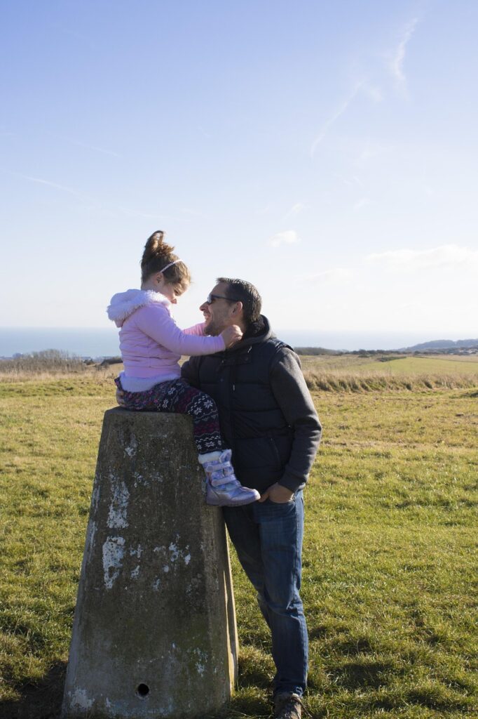 草原の中で父親と娘が笑顔で見つめ合う写真。親子の深い絆と温かな時間を表現。