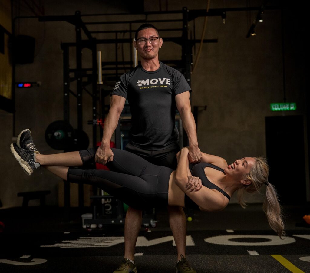 ジムで笑顔の男女が一緒に筋トレをしている様子。仲間と励まし合いながら続けるボディメイクの楽しさを表している。