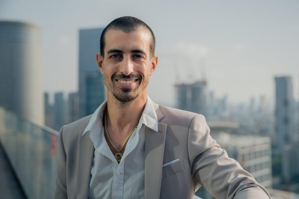 「午前中の光が差すビルの屋上でスーツ姿の40代男性が笑顔でポーズを決めている。再出発と自己信頼を象徴する姿。」