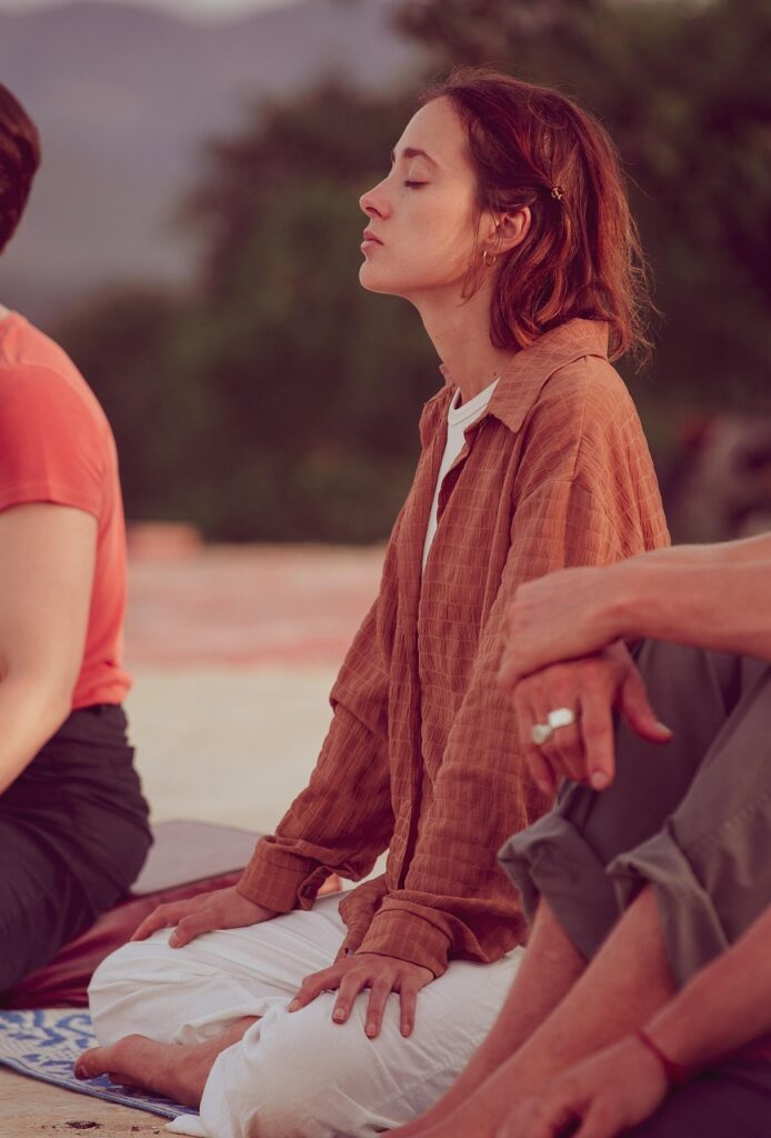 「朝方、屋外で瞑想する女性。穏やかな表情で目を閉じ、静かな時間の中で自分と向き合っている。」