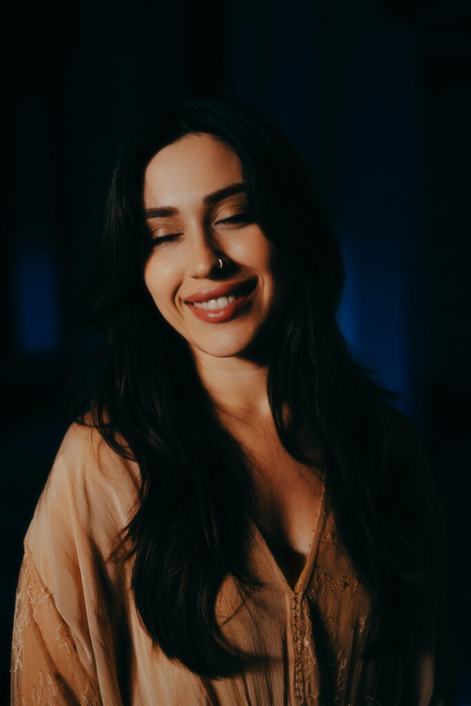 夜の柔らかい光の中で、目を閉じて微笑む女性。リラックスしながら心を整える様子を表した写真。