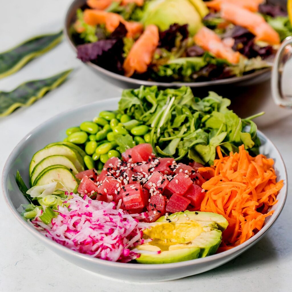 テーブルの上のサラダボウルに盛られた玉ねぎ、人参、豆、アボカドなどの野菜の写真。血糖値を上げにくくするヘルシーな夜ごはんのイメージ。