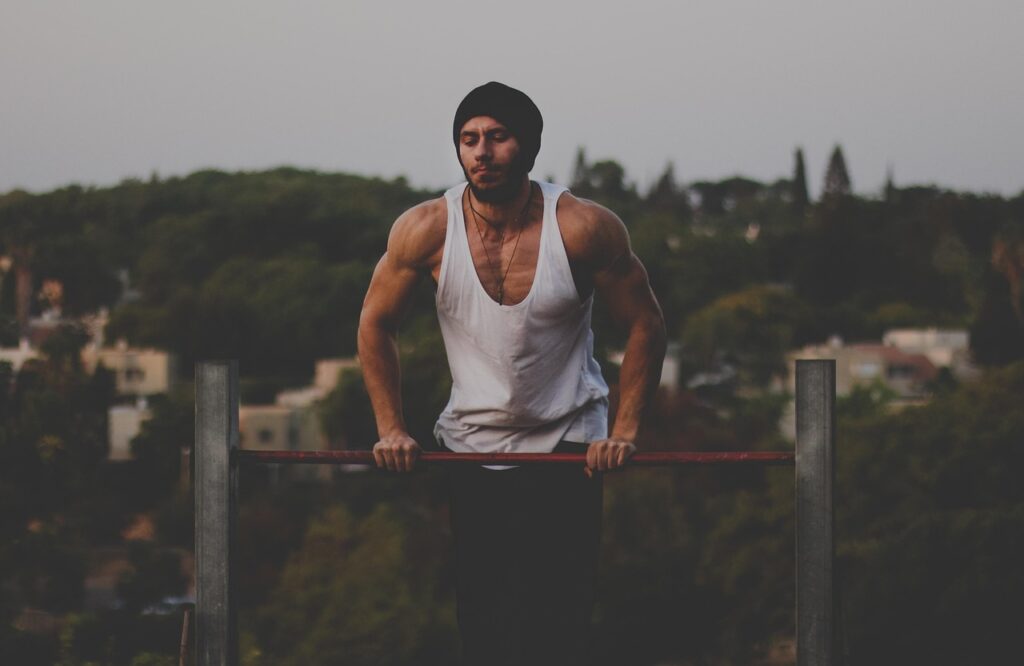 「公園の鉄棒で懸垂トレーニングを行う筋肉質な男性。たくましい背中と腕の筋肉が際立つシーン。」