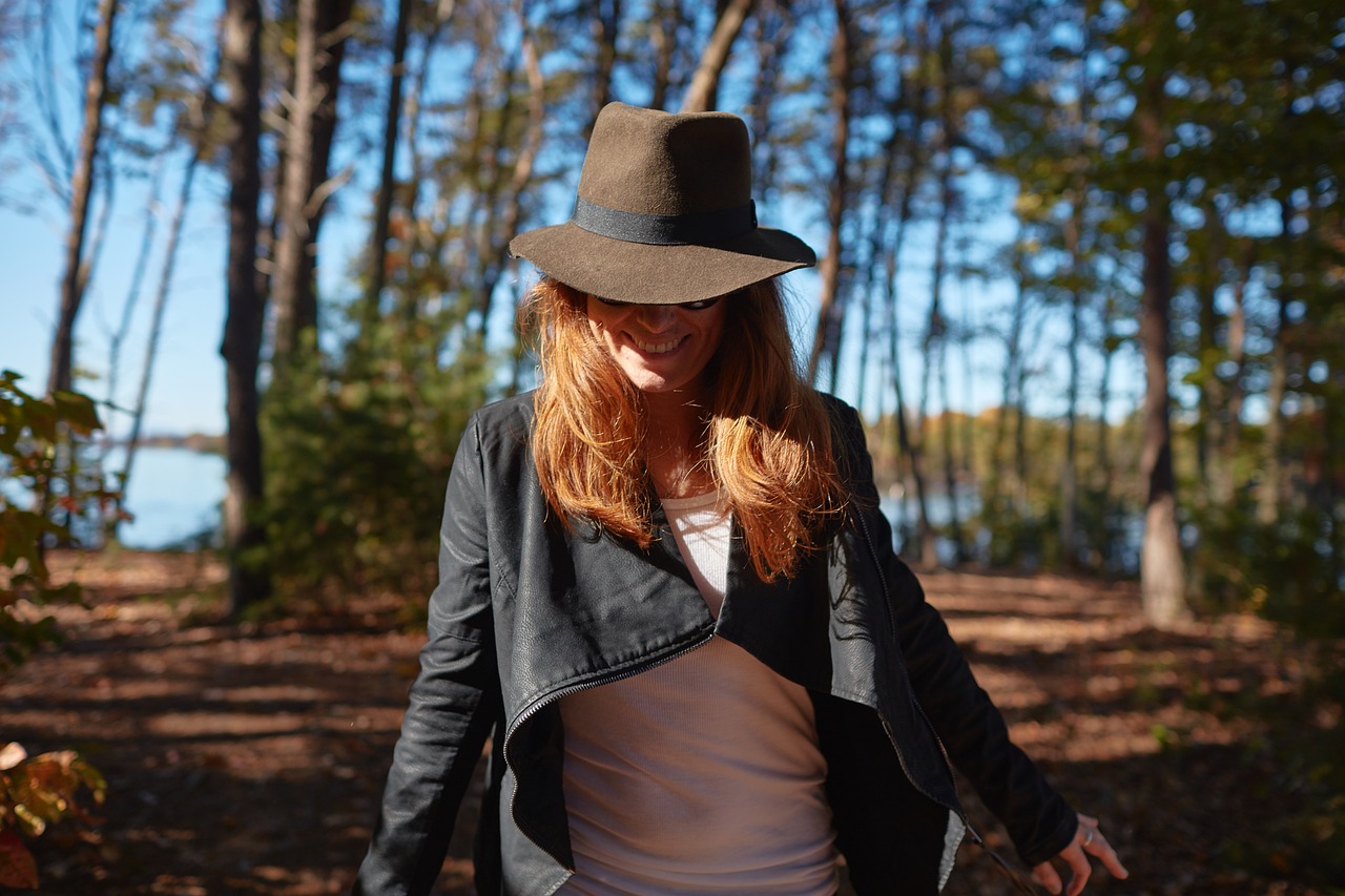 森の中で帽子をかぶり、笑顔で歩く女性の後ろ姿
