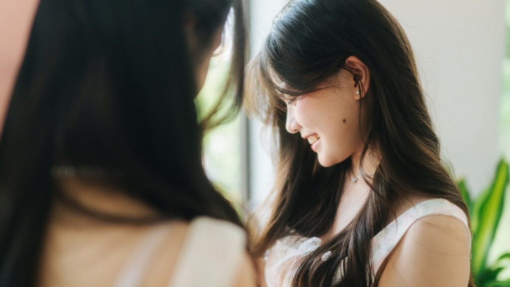 鏡に映る自分をやさしく見つめ、微笑む女性。自己イメージと内面の変化を象徴する一枚。