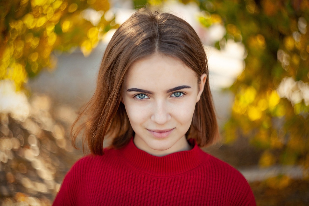 赤いセーターを着た女性が自然の中でこちらを見つめ、落ち着いた表情をしている写真。心の静けさと内側の強さを象徴するイメージ。