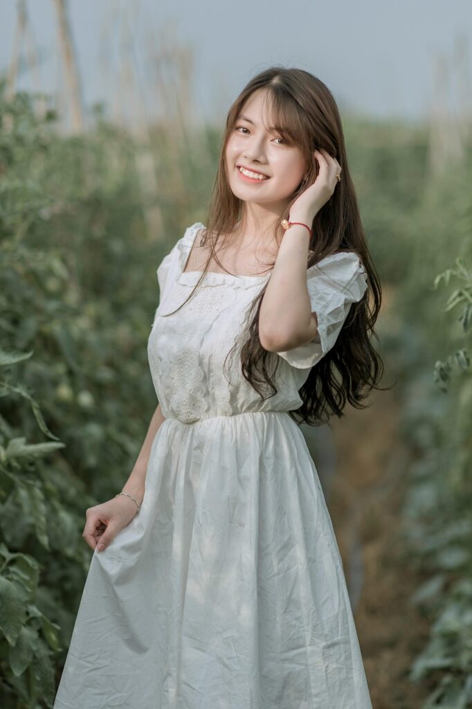 「白いワンピースを着た女性が畑でポーズを取り、笑顔でこちらを見ている。自然の中で自信と前向きさを感じさせる姿。」