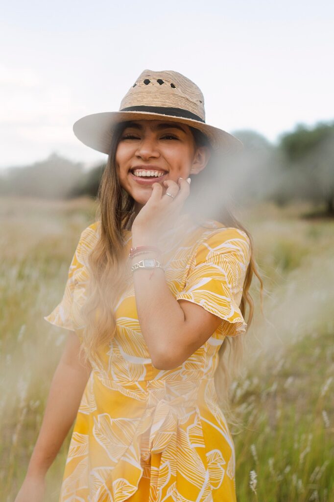 「草原に立ち、黄色いワンピースを着て笑顔を見せる女性。希望と前向きな気持ちを象徴する姿。」