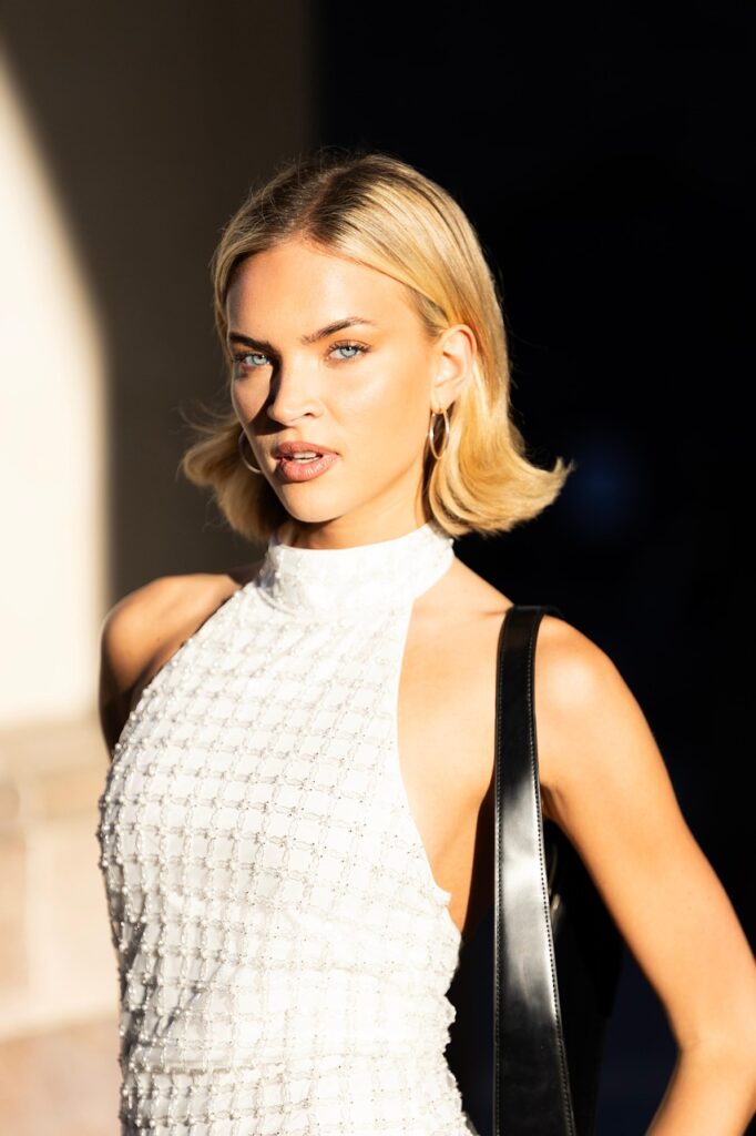 「街中で背筋を伸ばして立ち、姿勢よくカメラ目線で微笑む美しい女性モデルの写真。」