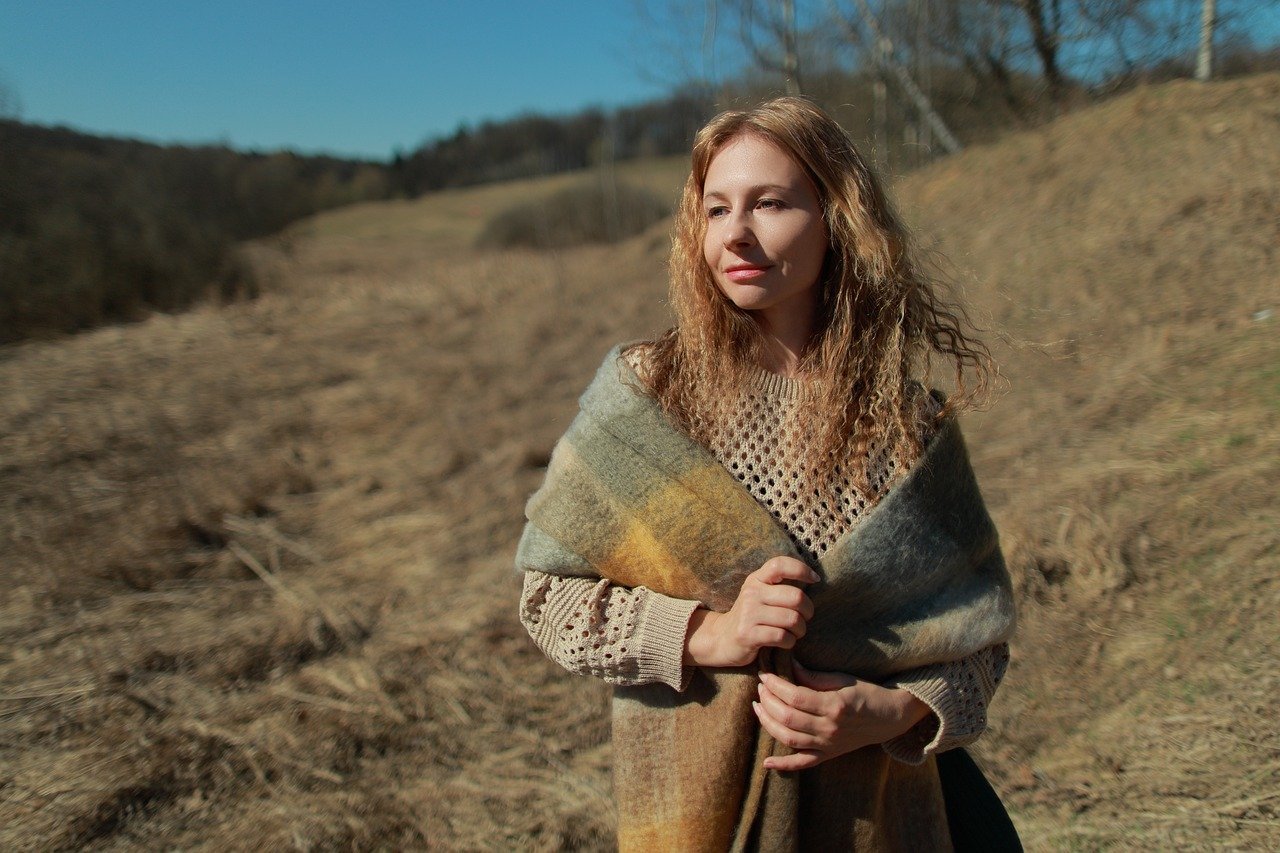 山の丘を下りながら歩く女性の後ろ姿。明るい陽光の中を一歩ずつ進む姿が、豊かさと前向きな変化を象徴している写真。