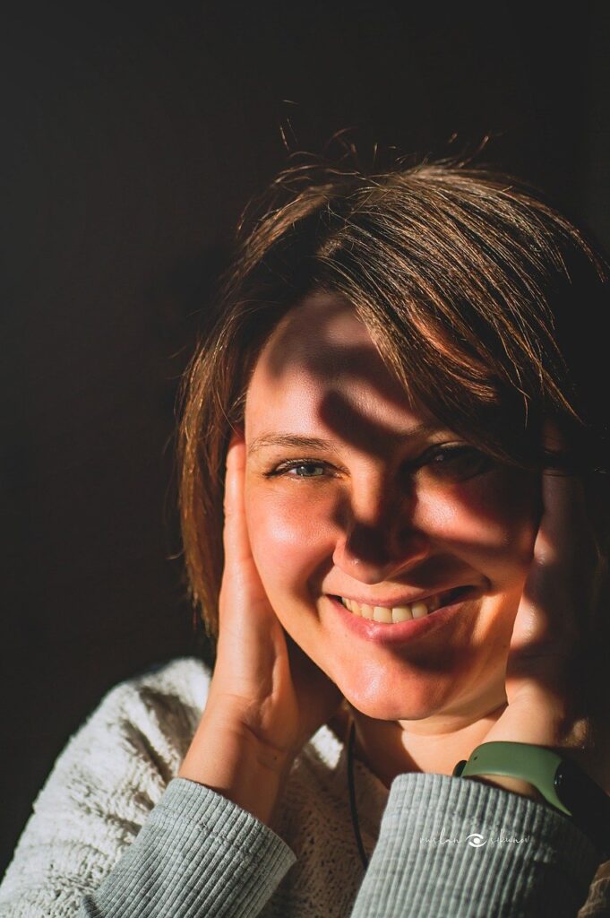 太陽の光を浴びながら、両手を顔に当てて微笑む女性の写真。前向きなエネルギーと幸福感を象徴している。