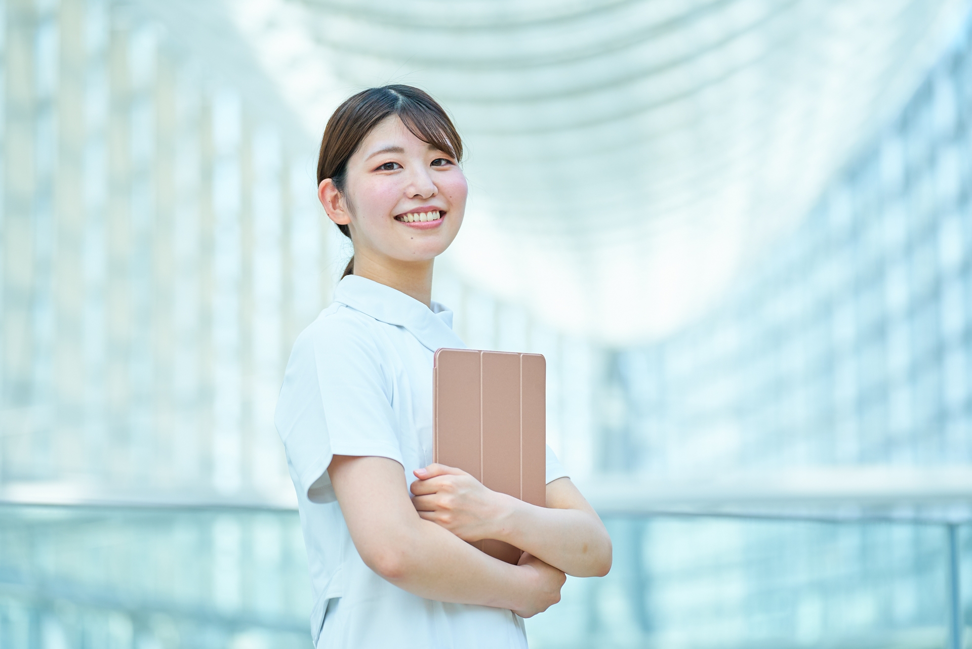 タブレットを持ちながら笑顔で立つ看護師の女性。キャリアアップや副収入を目指すイメージ
