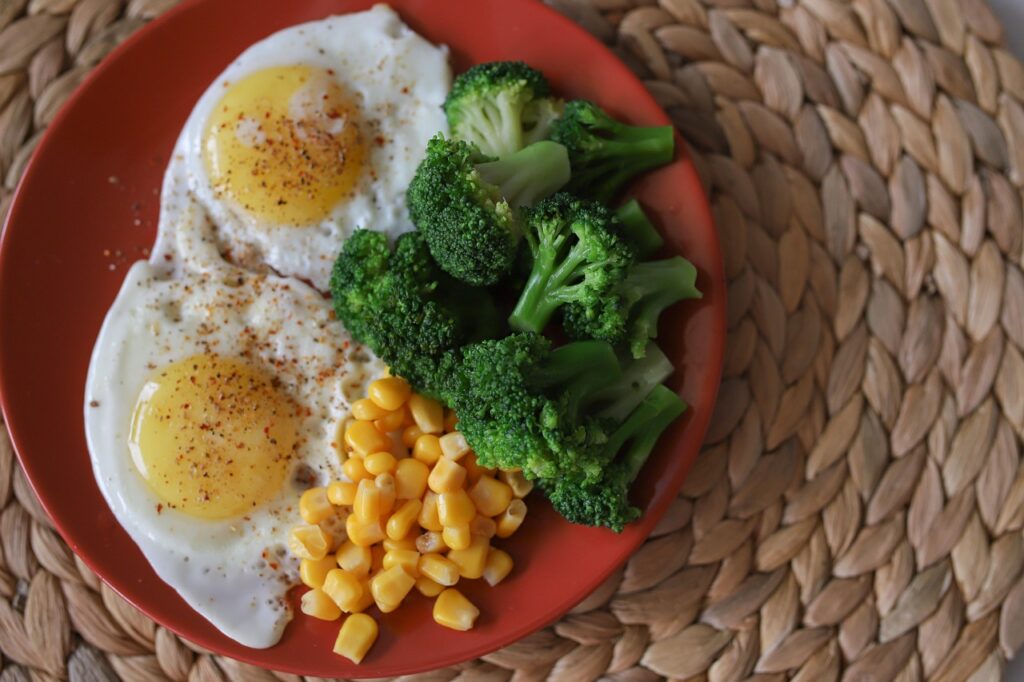 皿の上にブロッコリー、目玉焼き、コーンが盛り付けられた栄養バランスの良い食事。タンパク質と野菜中心のヘルシープレート。