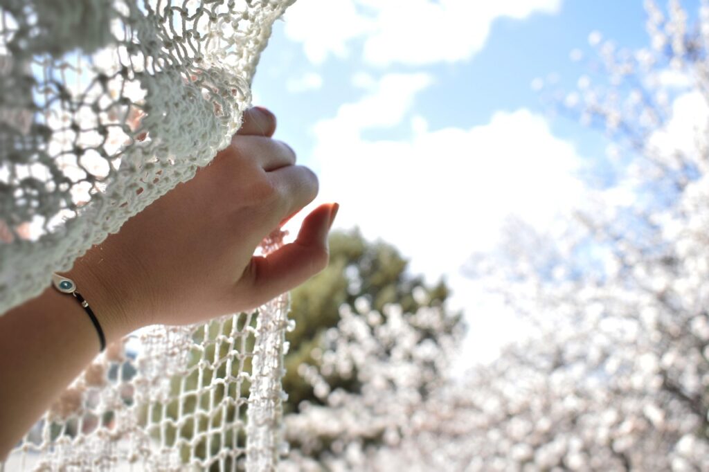 光の差し込むレースカーテンに手を添え、外を見つめる様子。人生を立て直すために無理に頑張らない選択を象徴する写真