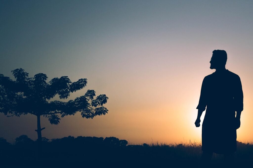夕日が射す大地で、大きな木を前に男性が立ち、シルエットになって木を見つめている写真。立ち直りや再出発を象徴している。