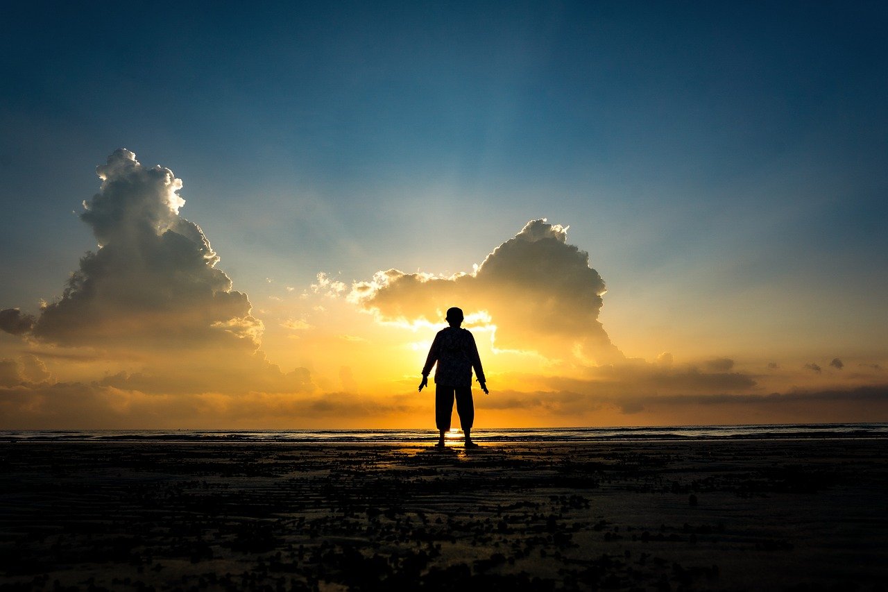 朝日が昇る浜辺で、一人静かに立ち人生を見つめ直す人物の後ろ姿