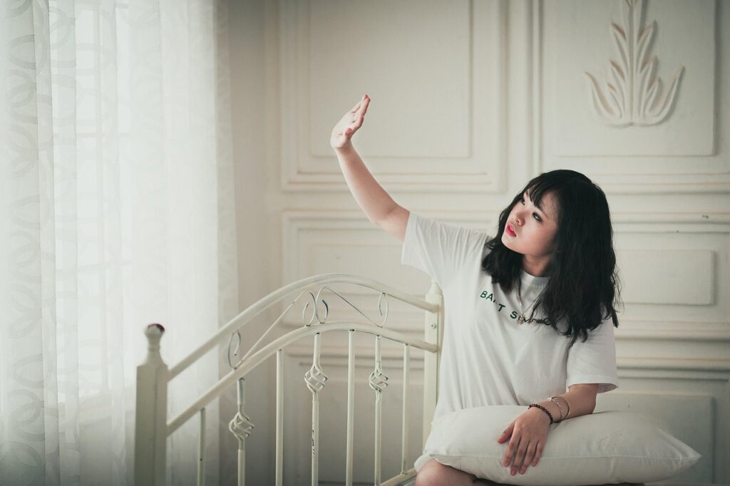 ベッドに座った女性が手を上げて制止するような仕草をしている様子。無理をせず、自分の心を守る境界線を表すイメージ。