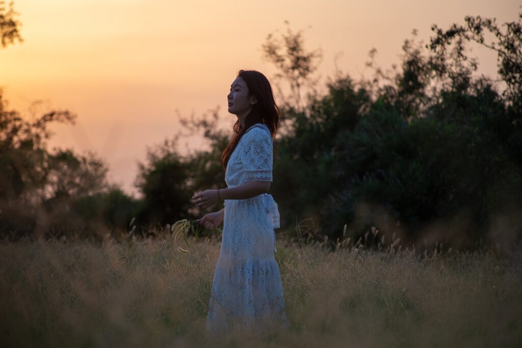 夕暮れの草原で立ち止まり、自分の気持ちと向き合う女性の後ろ姿
