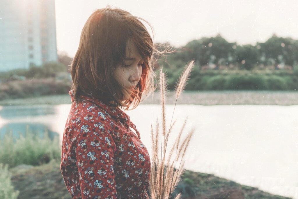 川辺で花束を手に、静かに立ち尽くす女性の後ろ姿。努力が報われない時間を象徴する写真