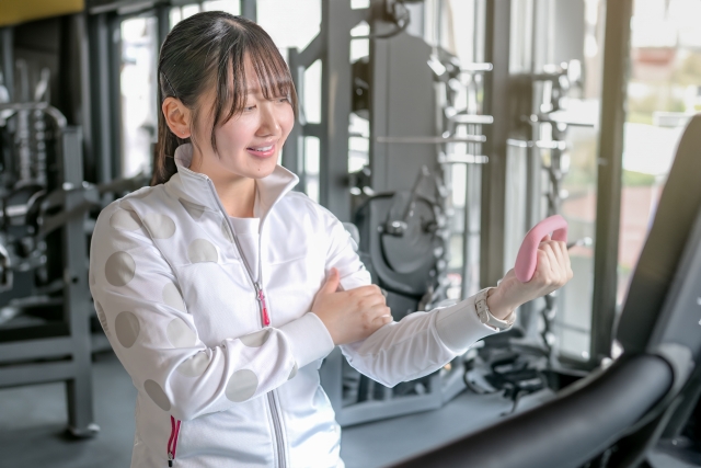 ジムで軽いダンベルを使いながら体をほぐす女性