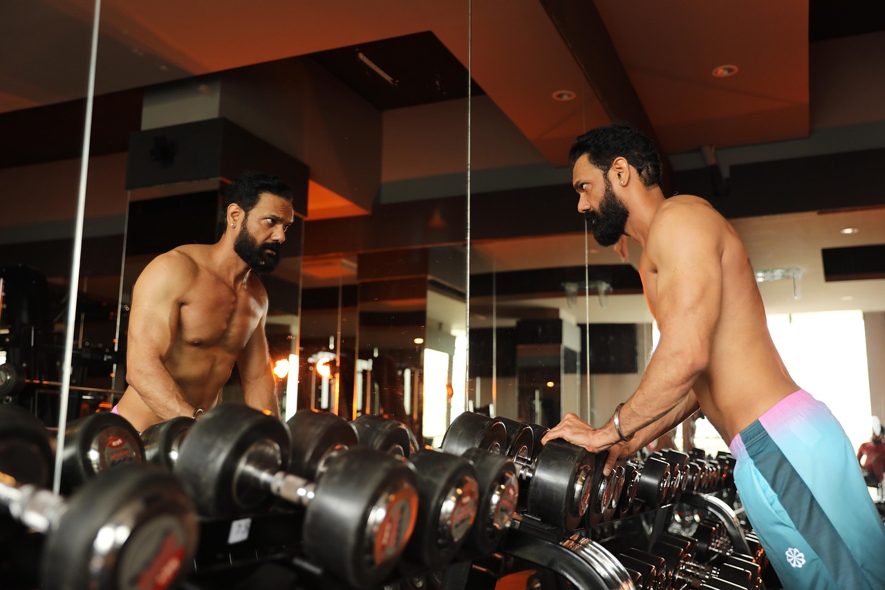 鏡の前でダンベルを見つめ、自分と向き合う40代男性の筋トレ風景