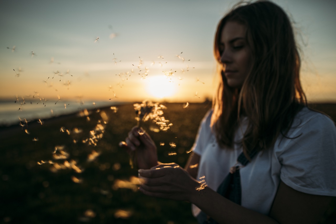 夕暮れの野原で光に包まれながら手の中の種を見つめる女性の姿