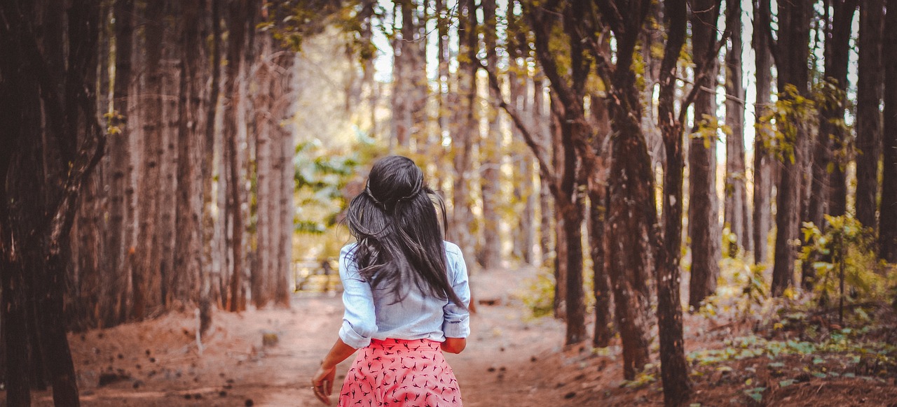 森の小道を一人で歩く後ろ姿の女性。変わらない日常の中でも前に進んでいる様子