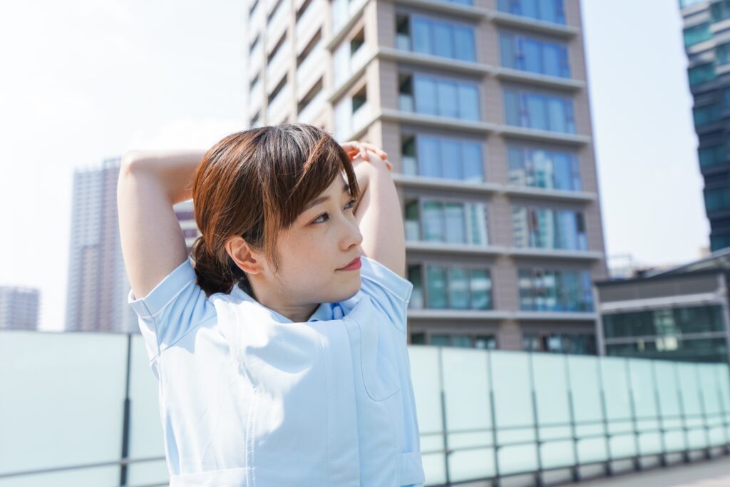 屋外で肩と腕を伸ばしてストレッチをする看護師の女性