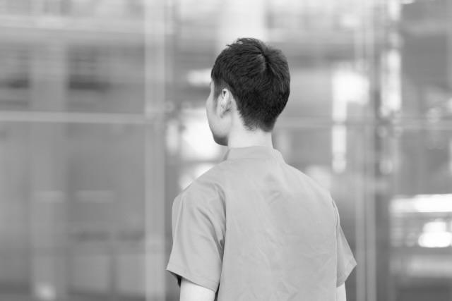 ガラス張りの建物を見つめる40代男性看護師の後ろ姿