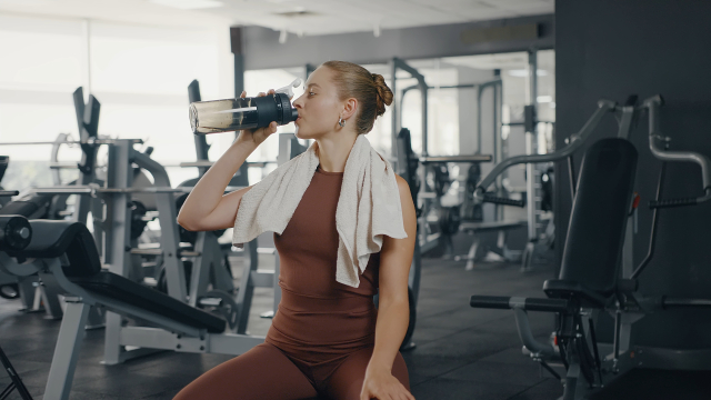 ジムでトレーニング後にシェイカーでドリンクを飲む女性