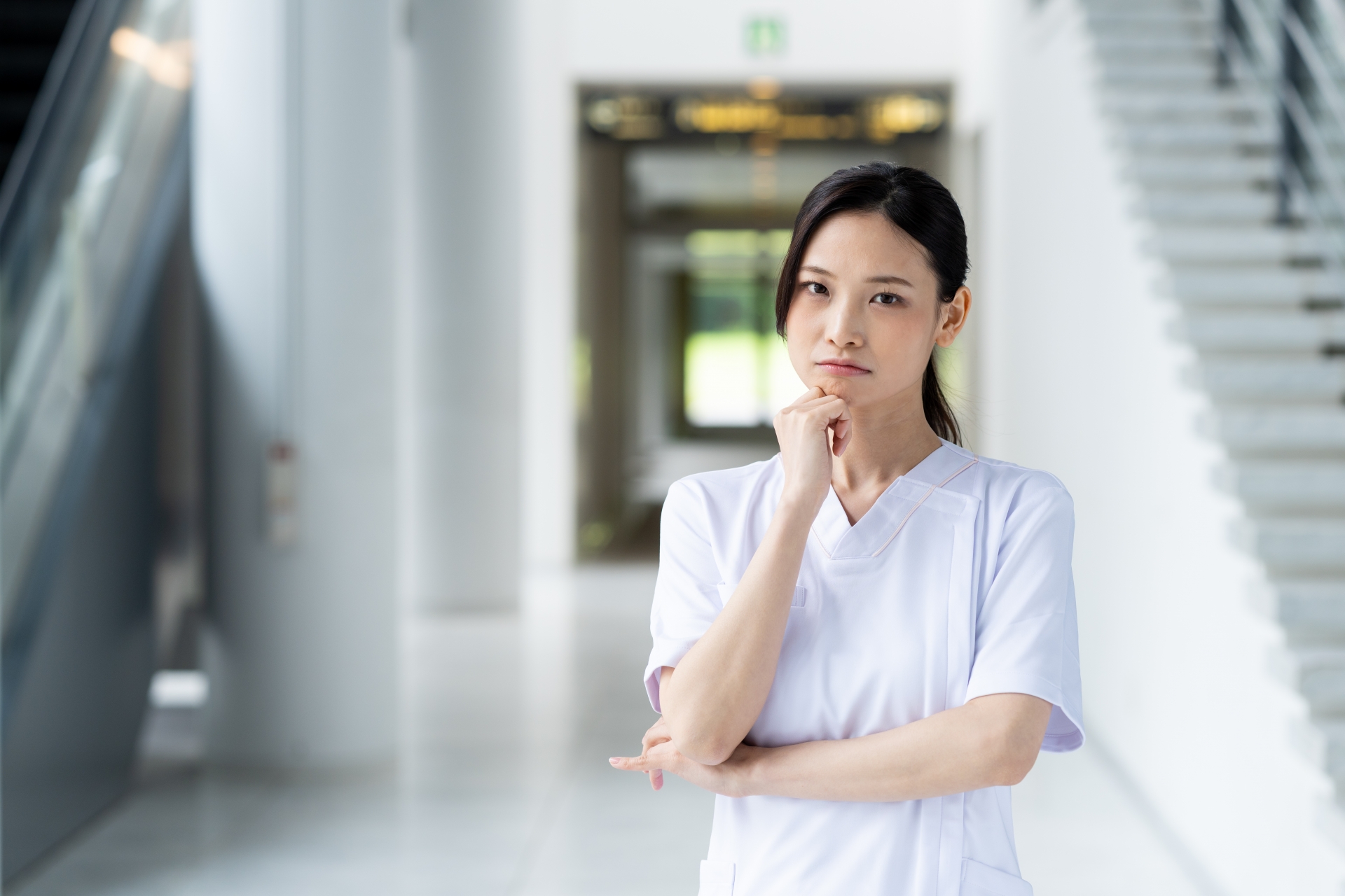 病院の廊下で腕を組みながら考え込む女性看護師の姿