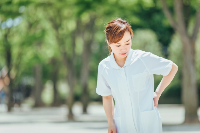 腰を押さえて痛みを感じている看護師の女性