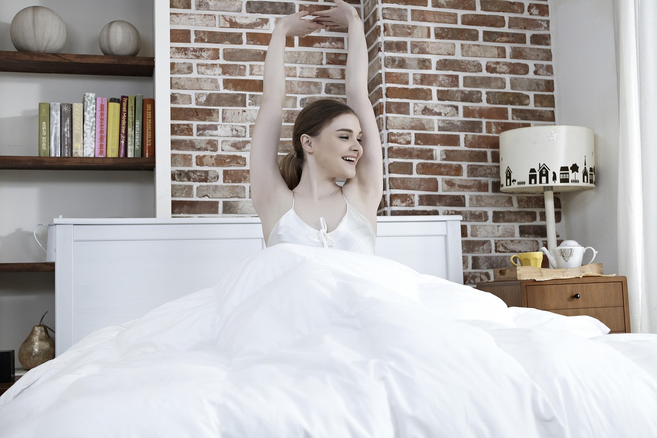 40代女性が朝ベッドで伸びをしている様子｜夜勤明けの回復イメージ