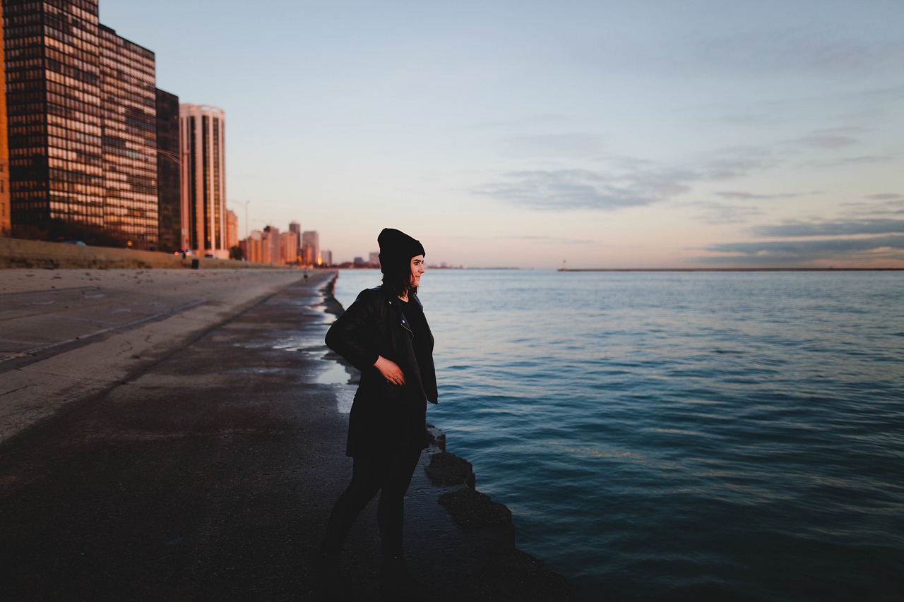 海辺に立ち、静かな海を見つめながら一人で考え込む女性の後ろ姿