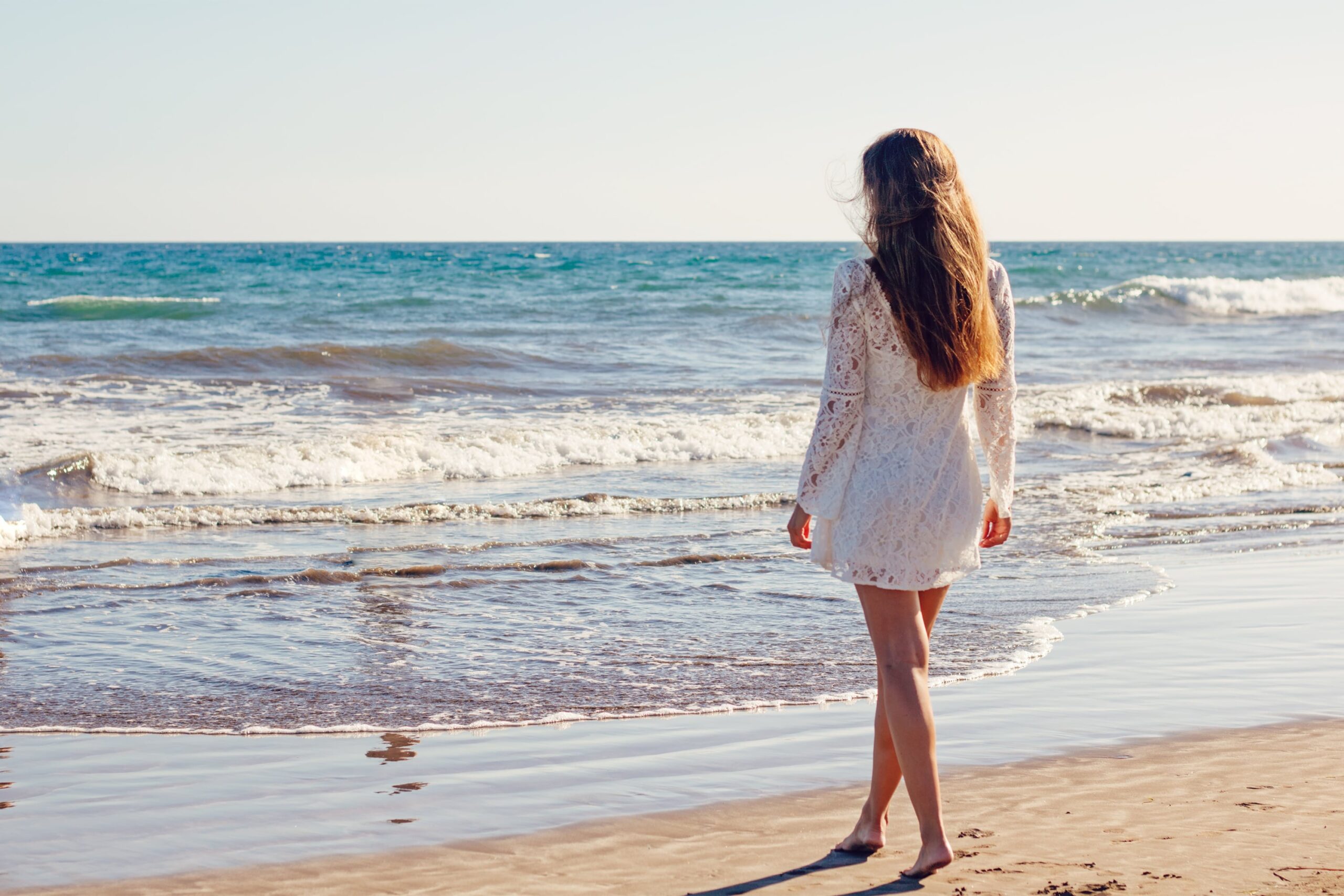 海辺を歩きながら一人で考える女性の後ろ姿