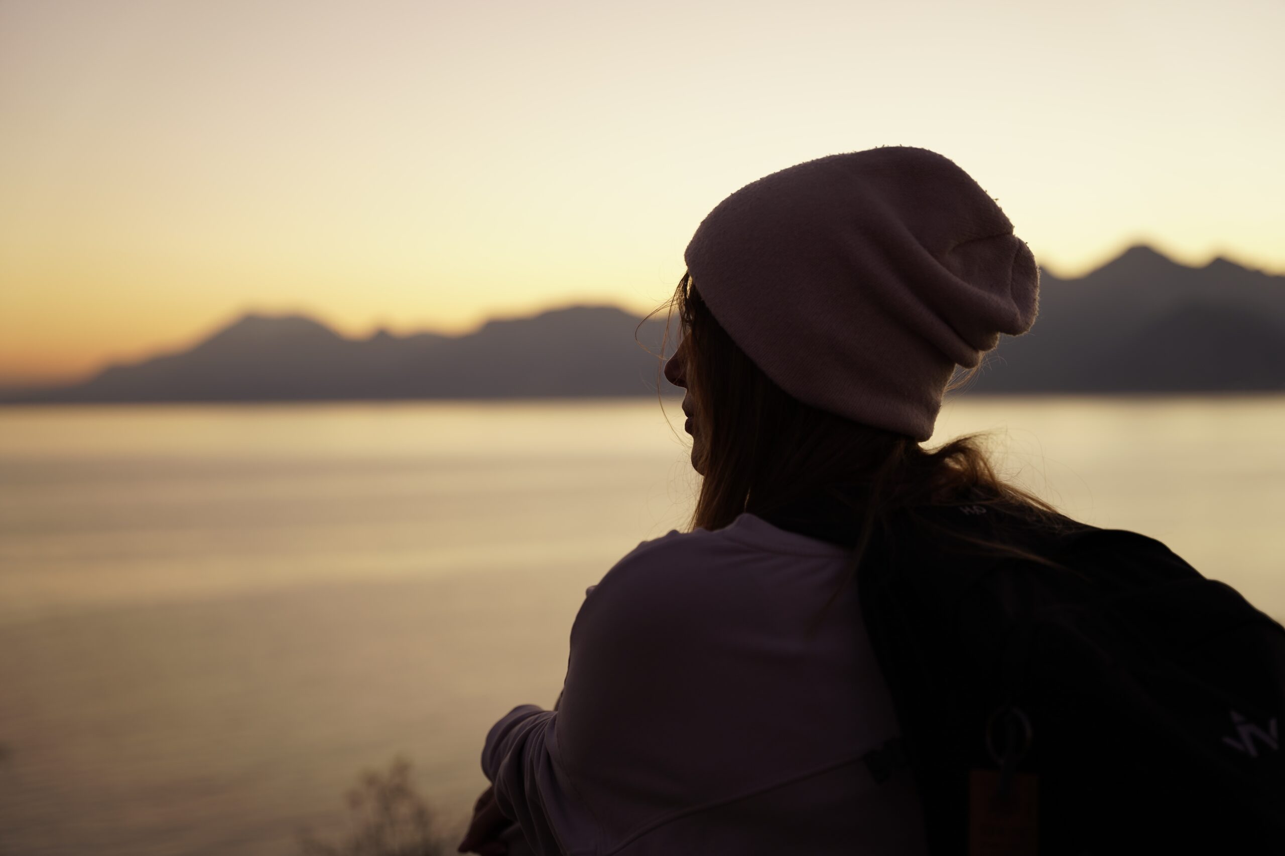 人生の失敗や後悔を振り返りながら、夕暮れの湖と山を静かに見つめる女性
